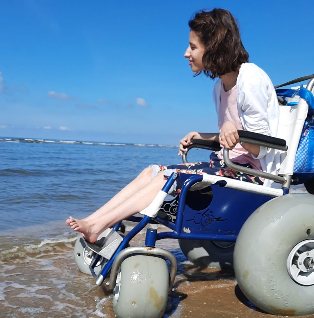 Dame op strand in een strandrolstoel.